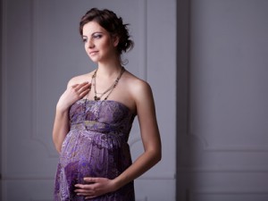 Eine schwangere Frau trägt ein langes, lilafarbenes Kleid