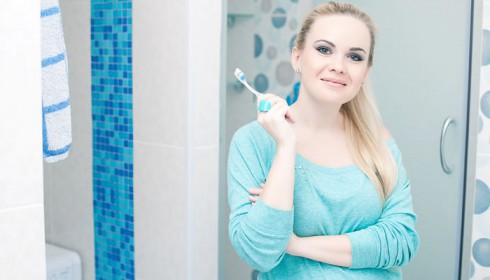 Eine hübsche Schwangere steht mit Zahnbürste vor dem Spiegel